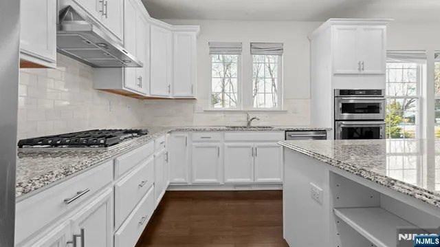 a kitchen with stainless steel appliances granite countertop a stove a sink a refrigerator and white cabinets with wooden floor