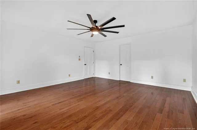 an empty room with wooden floor a ceiling fan and windows