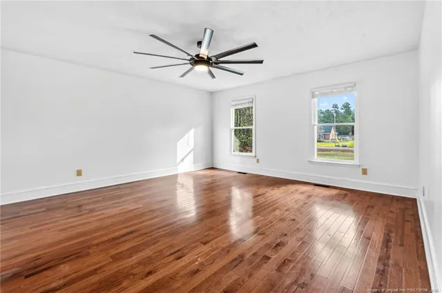 an empty room with wooden floor fan and windows