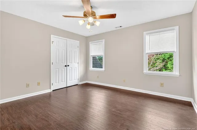an empty room with wooden floor chandelier fan and windows