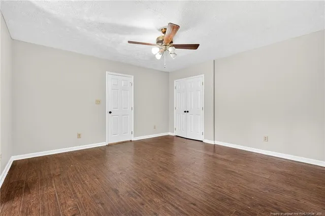 an empty room with wooden floor ceiling fan and windows