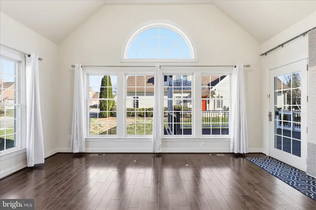an empty room with wooden floor and windows with curtains