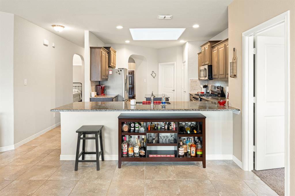 916 Falcon Road Argyle, TX 76226 - Photo 17 of 37 Kitchen with dark stone countertops, stainless steel appliances, kitchen peninsula, and a kitchen bar