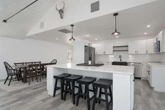 a kitchen with stainless steel appliances kitchen island granite countertop a dining table chairs and white cabinets