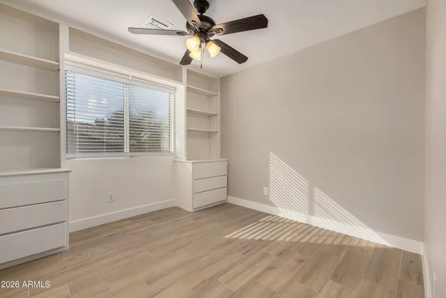 an empty room with wooden floor fan and windows