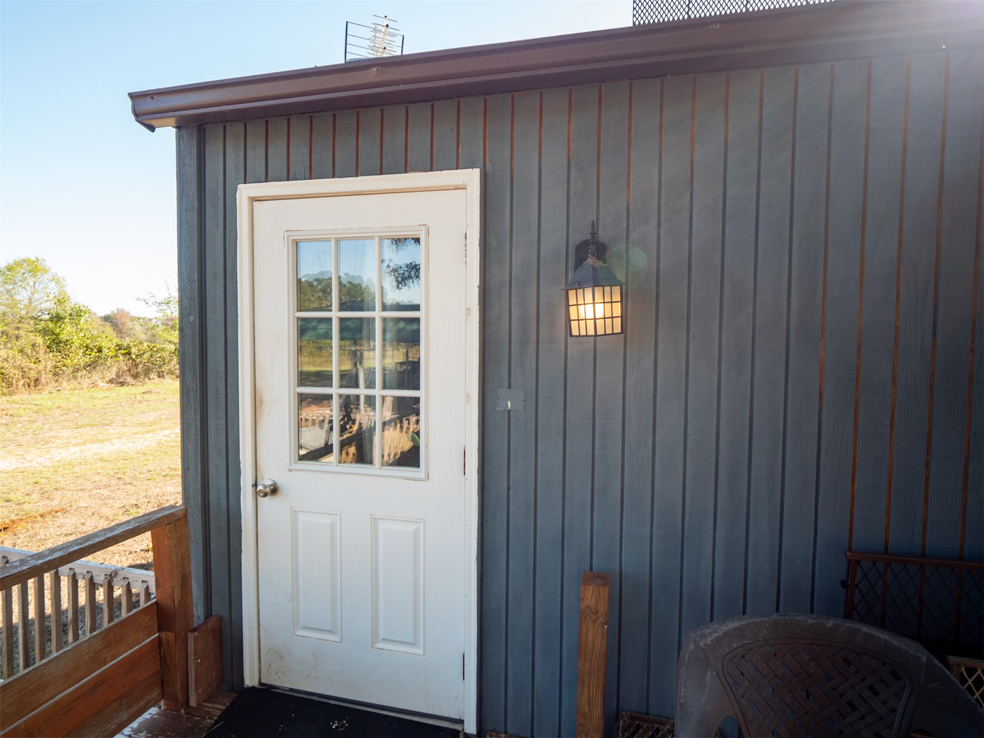 1599 North 4010 Road Boswell, OK 74727 - Photo 54 of 57 White paneled door with glass inserts, exterior wall sconce, vertical plank siding, and a partial wooden railing of Bunk House