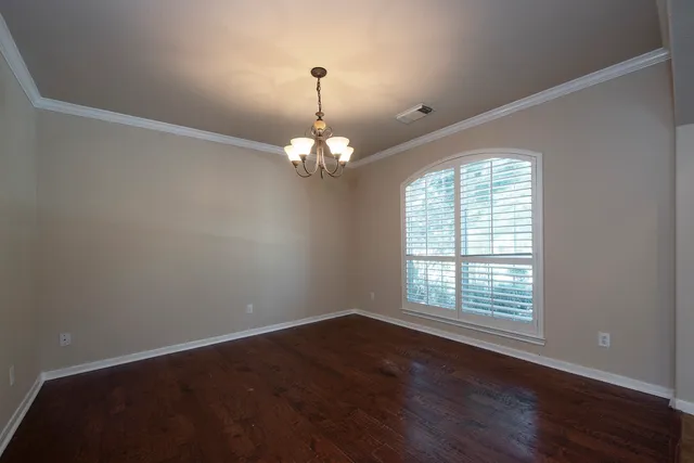 an empty room with wooden floor chandelier and windows
