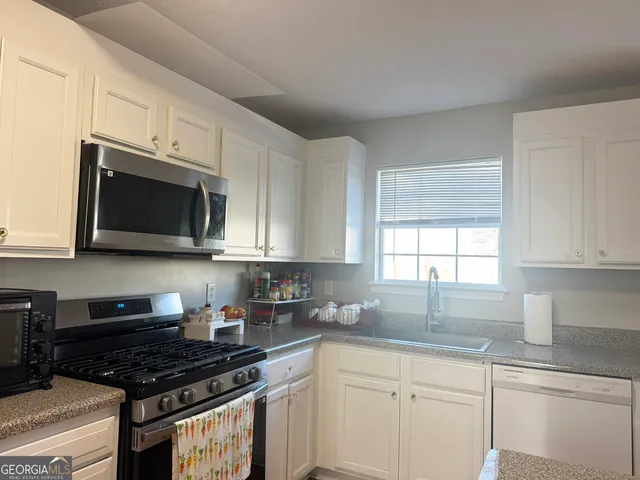 a kitchen with stainless steel appliances a sink a stove a microwave cabinets and a window