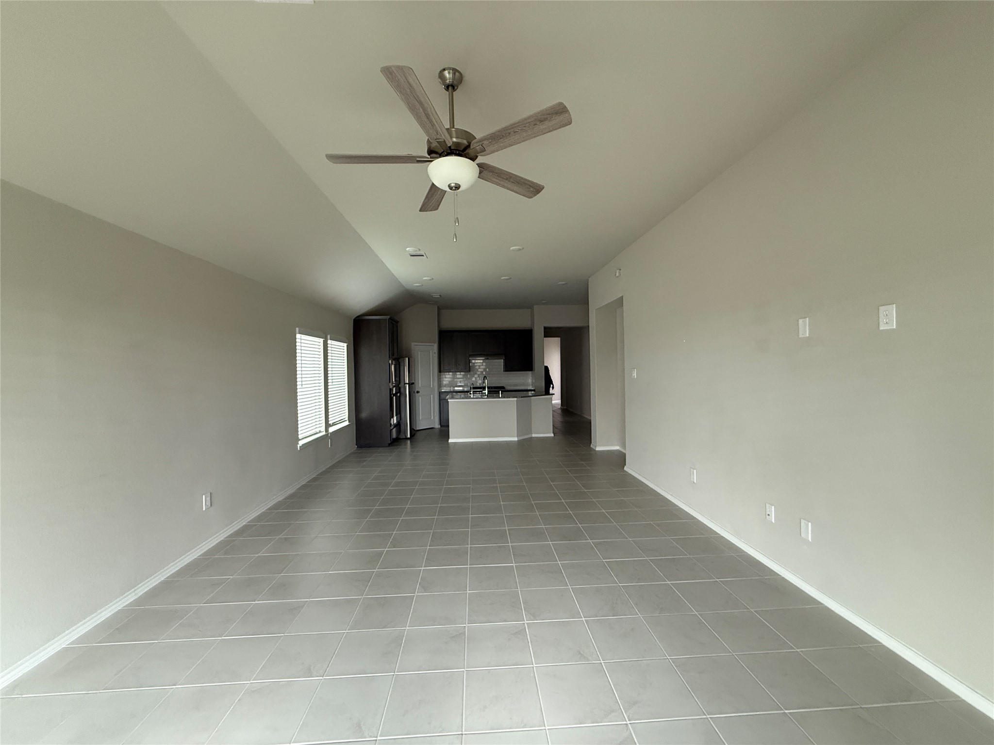 31961 Retama Rnch Drive Spring, TX 77386 - Photo 13 of 25 This spacious room features a modern open layout with light gray tiled floors and neutral walls, leading into a well-lit kitchen area with stainless steel appliances. A ceiling fan adds comfort to the space.