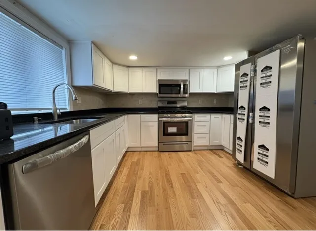 a kitchen with stainless steel appliances granite countertop a refrigerator a sink dishwasher a stove top oven a refrigerator and cabinets with wooden floor
