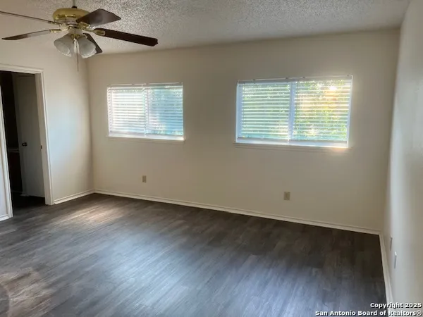 an empty room with wooden floor fan and windows