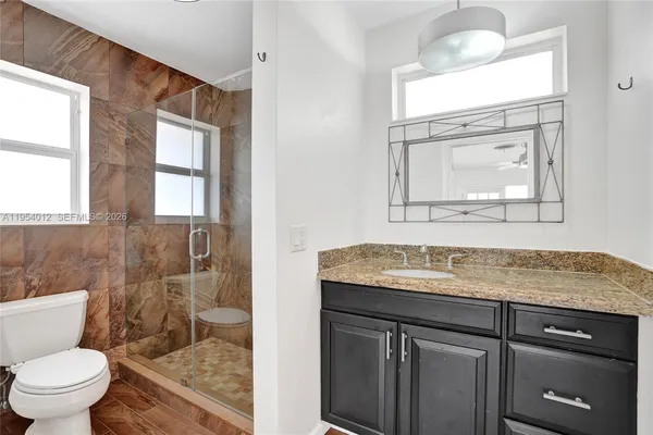 a bathroom with a granite countertop sink vanity mirror and toilet