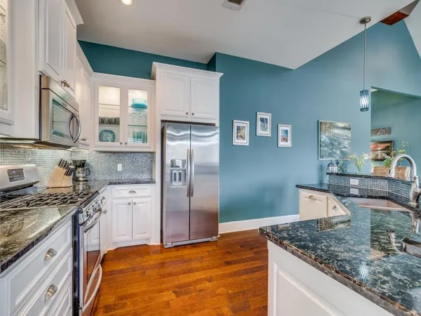 a kitchen with stainless steel appliances granite countertop a stove top oven a refrigerator a sink and chairs with wooden floor