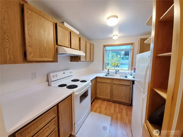 a kitchen with granite countertop a stove a sink dishwasher and a refrigerator with wooden floor