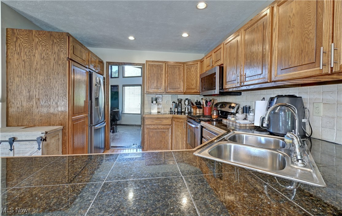 5747 Middle Run Road Dover, OH 44622 - Photo 5 of 30 Kitchen featuring brown cabinets, stainless steel appliances, decorative backsplash, a textured ceiling, and recessed lighting