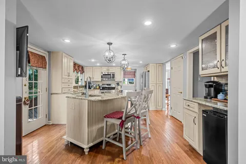 a kitchen with stainless steel appliances kitchen island granite countertop a refrigerator a stove a sink and white cabinets with wooden floor