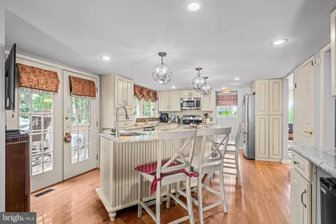 a kitchen with stainless steel appliances kitchen island granite countertop a refrigerator a stove top oven and a dining table with wooden floor
