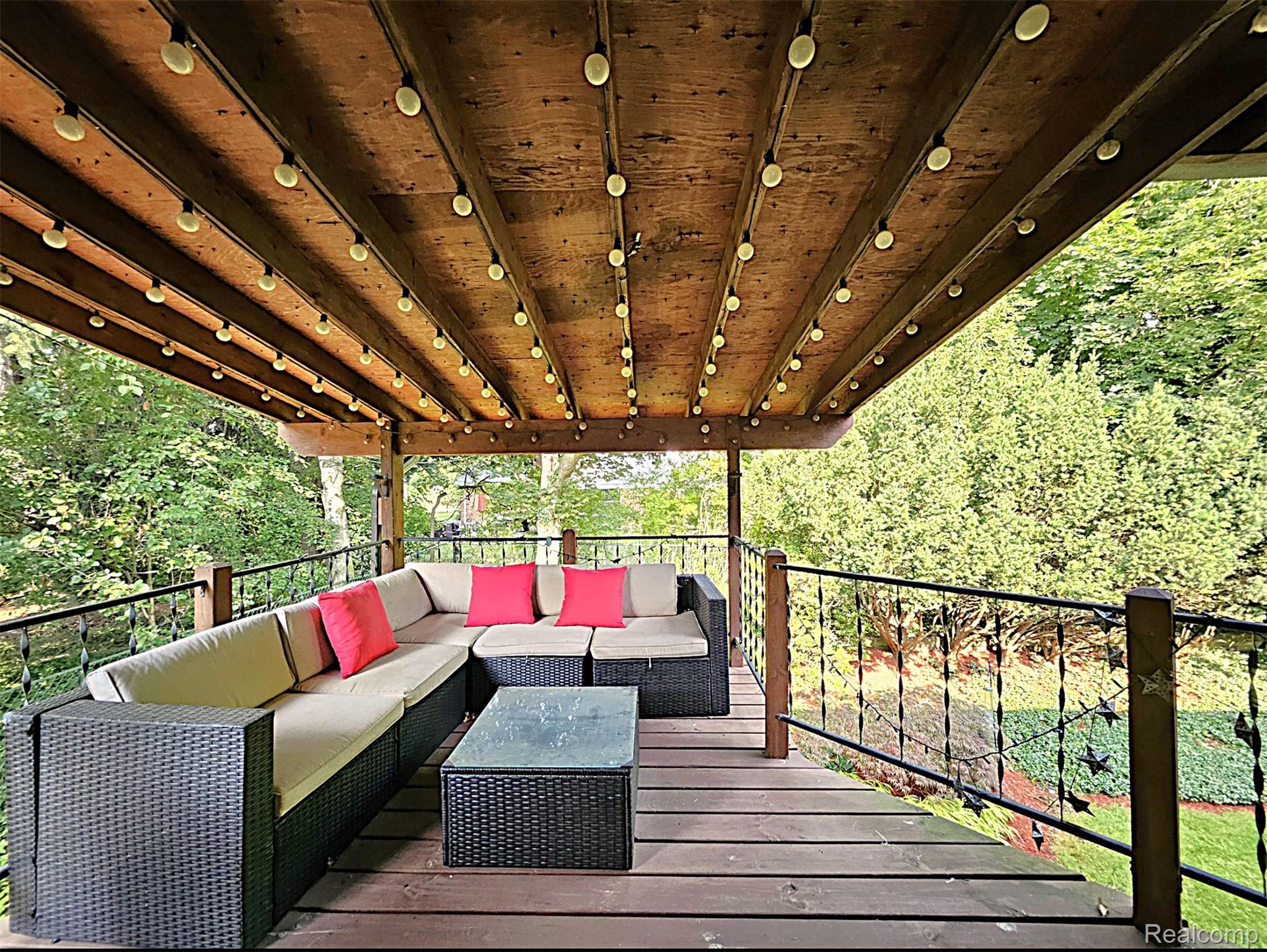 7120 Pebblecreek Road West Bloomfield, MI 48322 - Photo 4 of 31 Expansive covered deck featuring a wood-plank ceiling with integrated string lighting, wood-finish flooring, and decorative wrought iron railings