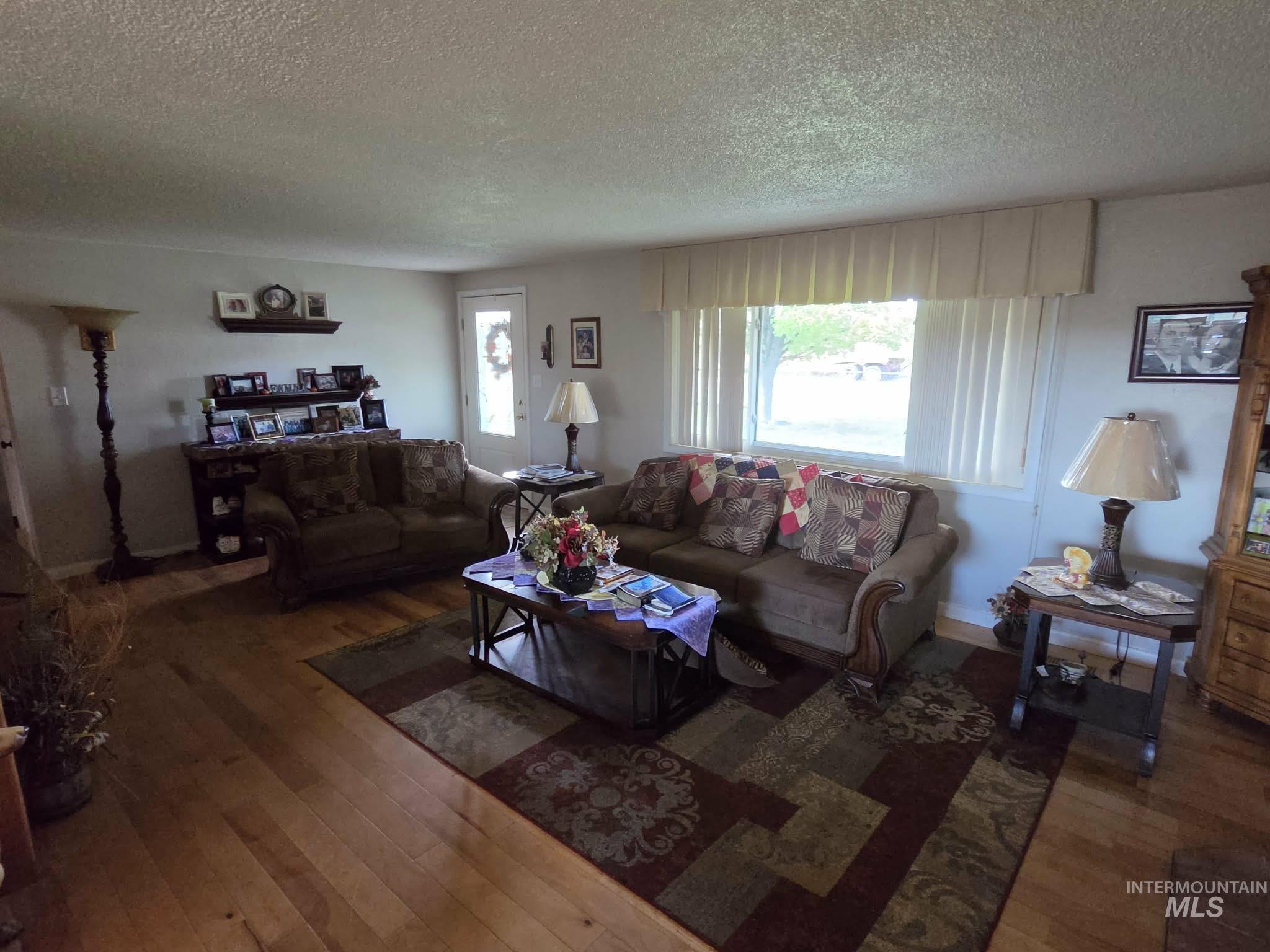 Bright living space featuring natural wood-finish flooring, a prominent window with horizontal blinds, and a built-in wall shelf