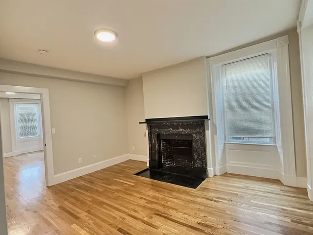 a view of an empty room with wooden floor fireplace and a window