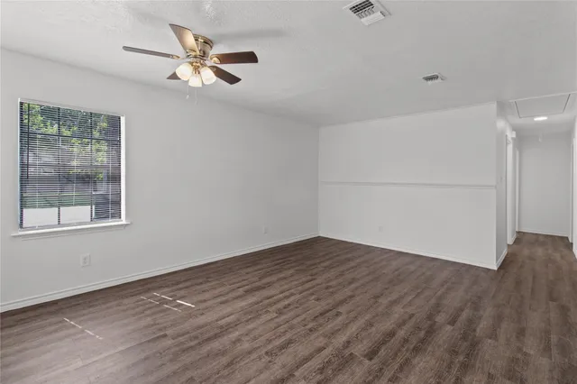 an empty room with wooden floor fan and windows