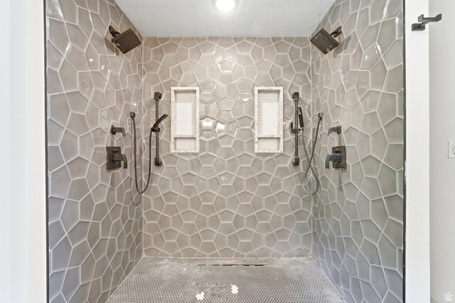 1410 Sumac Drive Logan, UT 84321 - Photo 16 of 28 Walk-in shower featuring geometric tiled walls, dual overhead rain showerheads, two handheld shower wands, integrated shelving niches, and dark bronze fixtures