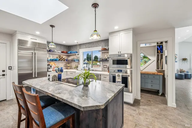 a kitchen with stainless steel appliances kitchen island granite countertop a dining table chairs and refrigerator