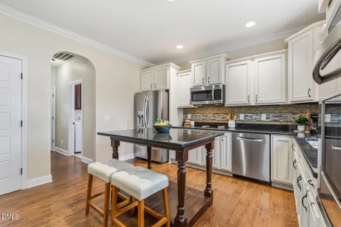 a kitchen with stainless steel appliances granite countertop a stove a refrigerator a microwave a sink and white cabinets with wooden floor