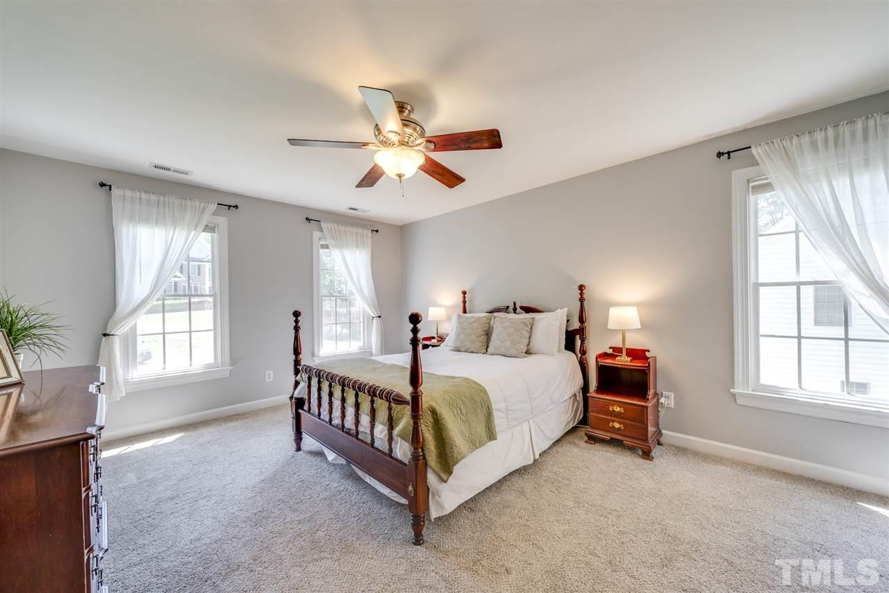 11921 Larka Court Raleigh, NC 27613 - Photo 14 of 30 a spacious bedroom with a bed a chandelier and windows