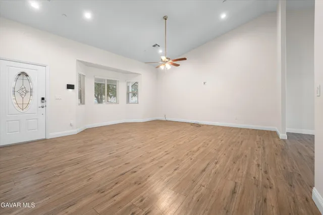 an empty room with wooden floor chandelier fan and windows