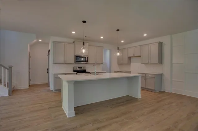 a view of an empty room and kitchen with wooden floor