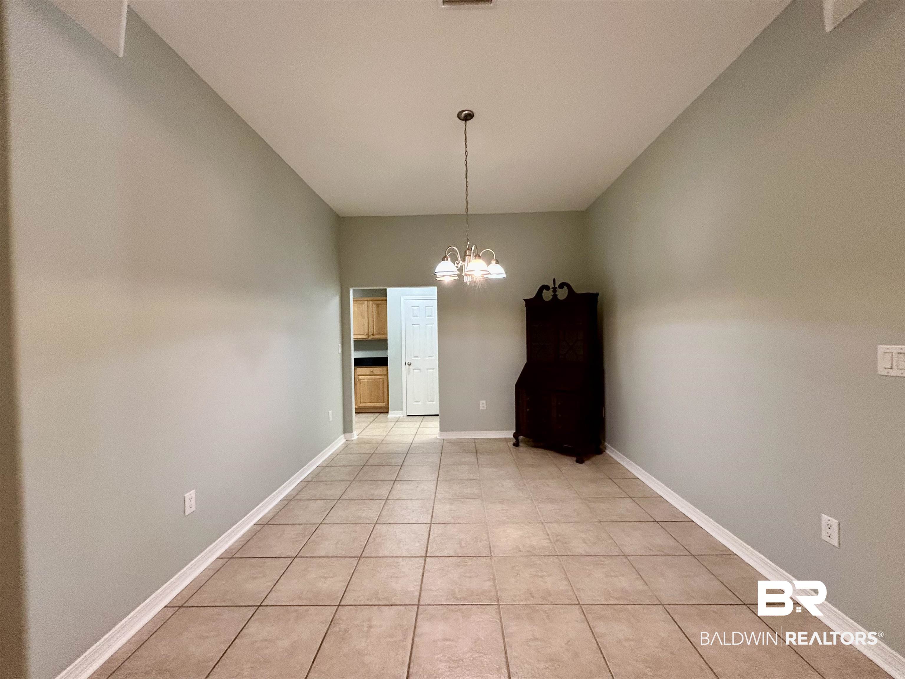 7198 Raintree Lane Gulf Shores, AL 36542 - Photo 9 of 33 Spacious room featuring neutral tone walls, tile flooring, a chandelier lighting fixture, and white baseboards