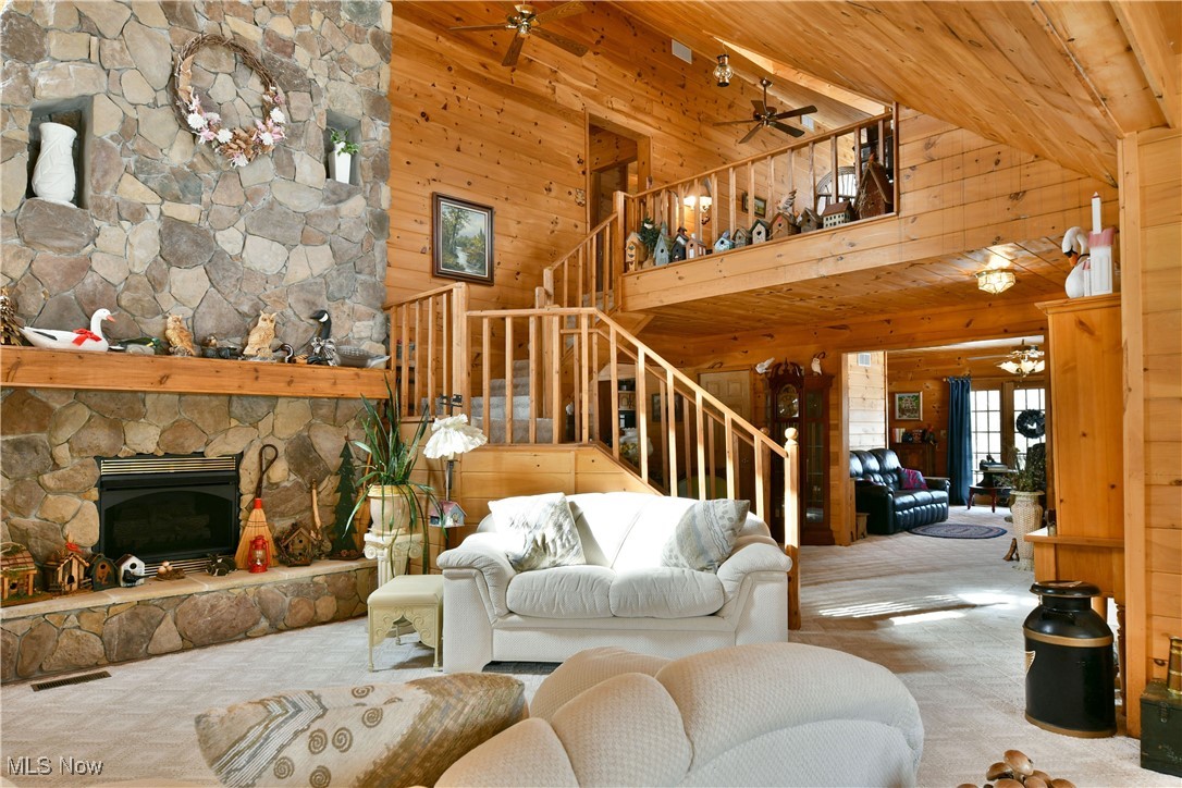 3339 Bushnell Campbell Road Fowler, OH 44418 - Photo 8 of 50 Living room featuring light carpet, wooden walls, a ceiling fan, stairs, and a stone fireplace