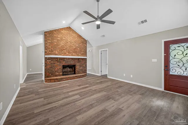 an empty room with windows a fireplace a ceiling fan and wooden floor