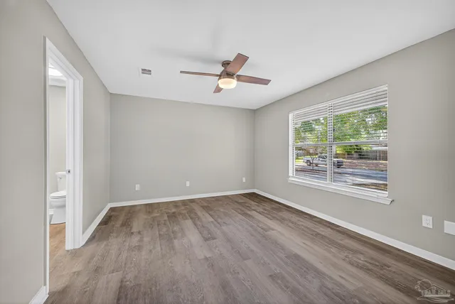an empty room with wooden floor ceiling fan and windows
