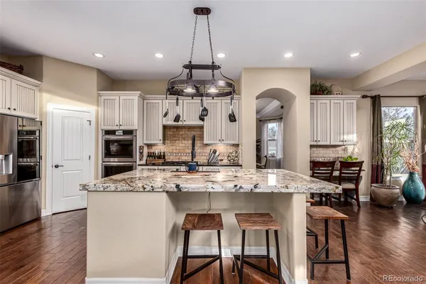 a kitchen with stainless steel appliances kitchen island granite countertop a refrigerator a stove top oven a sink dishwasher and white cabinets with wooden floor