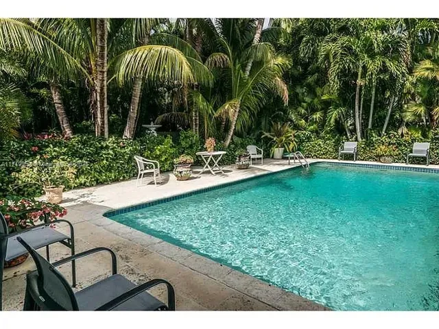 a view of a swimming pool with a lawn chairs under palm trees
