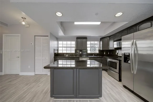 a kitchen with kitchen island granite countertop a sink cabinets and stainless steel appliances