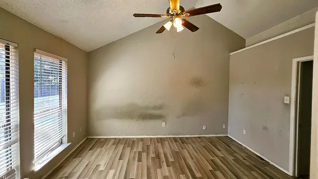 an empty room with wooden floor fan and windows