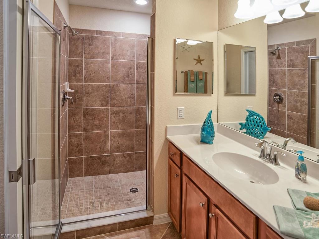 9560 Trevi Court, Unit 4842 Naples, FL 34113 - Photo 11 of 25 a bathroom with a granite countertop sink a mirror and a shower