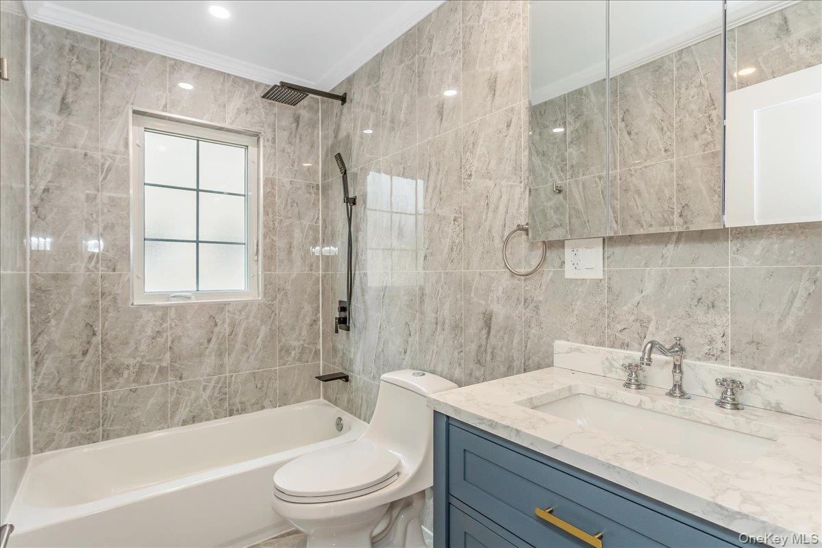 243-36 Caney Road Queens, NY 11422 - Photo 15 of 30 Bathroom with bathing tub / shower combination, tile walls, vanity, and ornamental molding