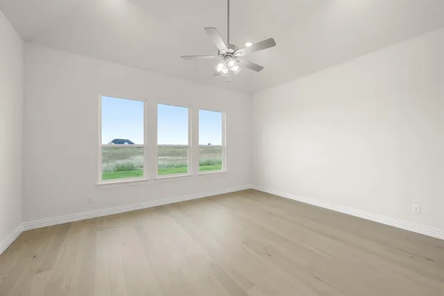 an empty room with wooden floor fan and windows