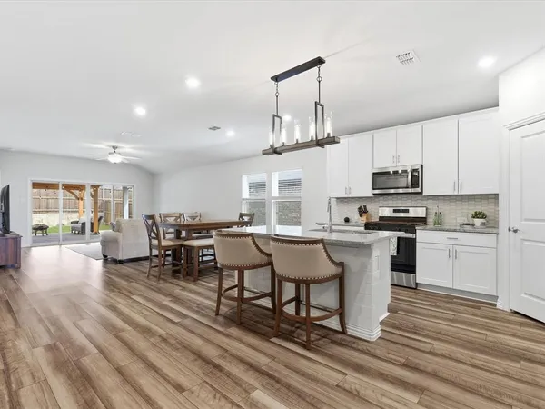 a open kitchen with stainless steel appliances granite countertop a stove a sink dishwasher a microwave oven with a dining table and chairs with wooden floor