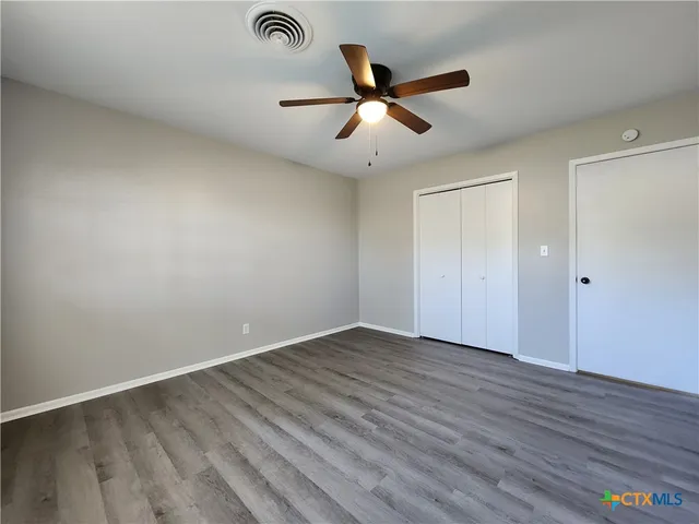 an empty room with wooden floor fan and windows