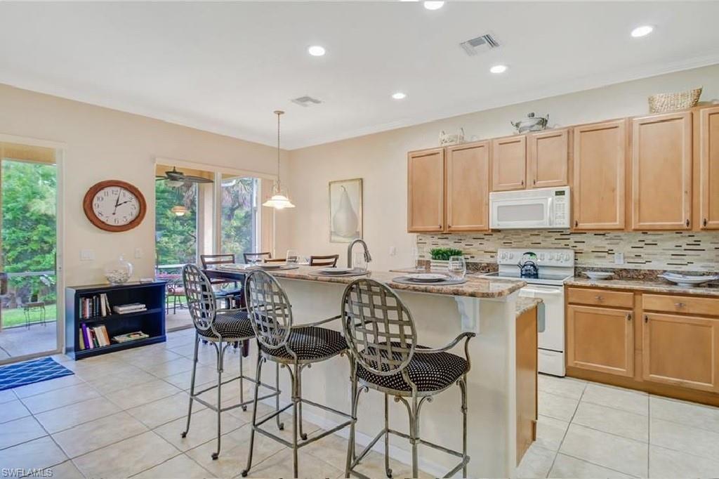 5706 Lago Villaggio Way Naples, FL 34104 - Photo 16 of 32 a kitchen with stainless steel appliances granite countertop a table and chairs in it
