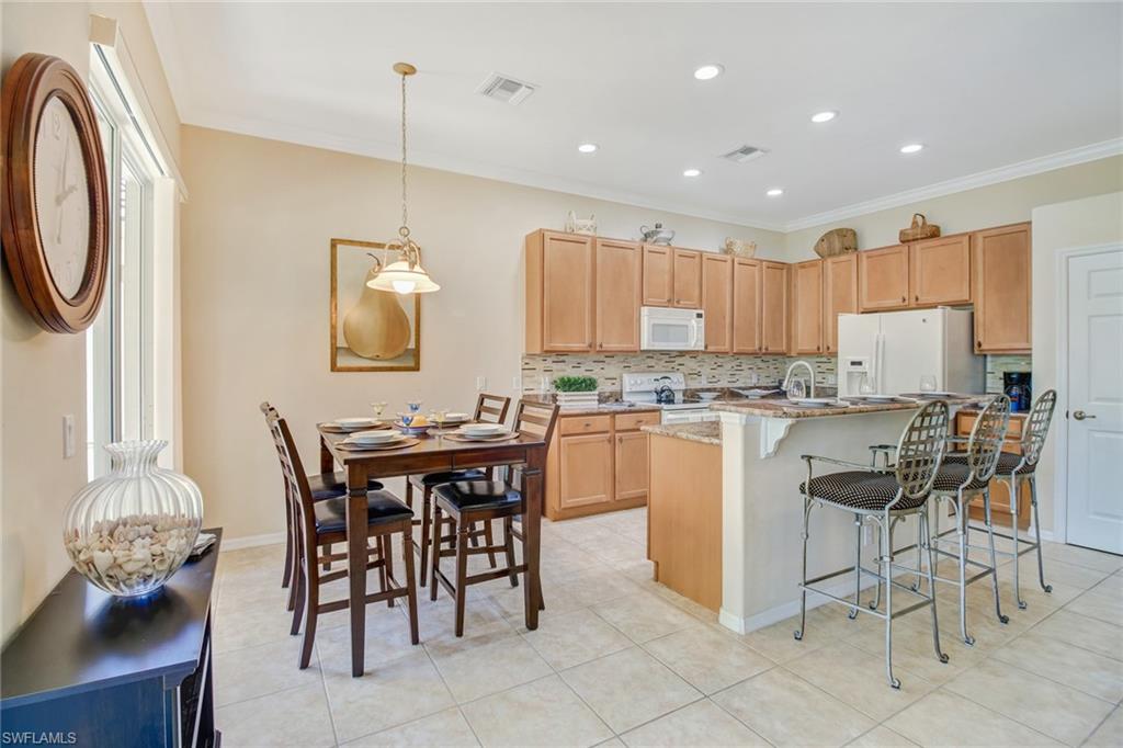 5706 Lago Villaggio Way Naples, FL 34104 - Photo 21 of 32 a kitchen with stainless steel appliances granite countertop a table and chairs in it