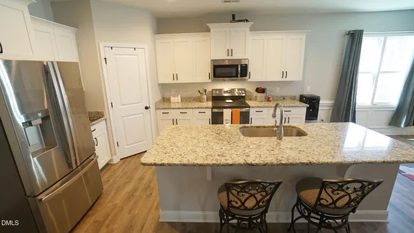 a kitchen with stainless steel appliances granite countertop a dining table chairs refrigerator and microwave
