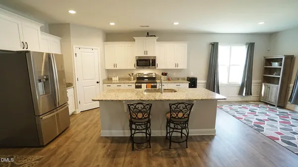 a kitchen with stainless steel appliances granite countertop a dining table chairs refrigerator and microwave