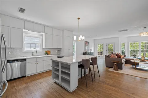 a open kitchen with white cabinets a sink dishwasher a dining table and chairs with wooden floor