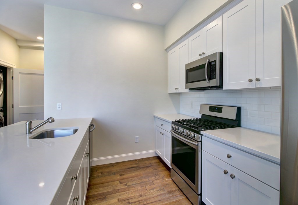 4 Kemp Street, Unit 4 Boston, MA 02127 - Photo 26 of 40 a kitchen with stainless steel appliances granite countertop a sink and a stove top oven with wooden floor